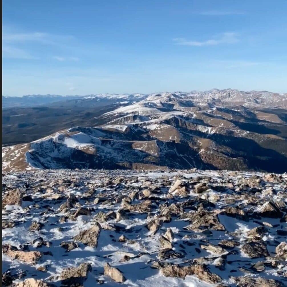 Rocky, snow-dusted mountain landscape under a clear blue sky, with rugged peaks and ridges extending into the distance.